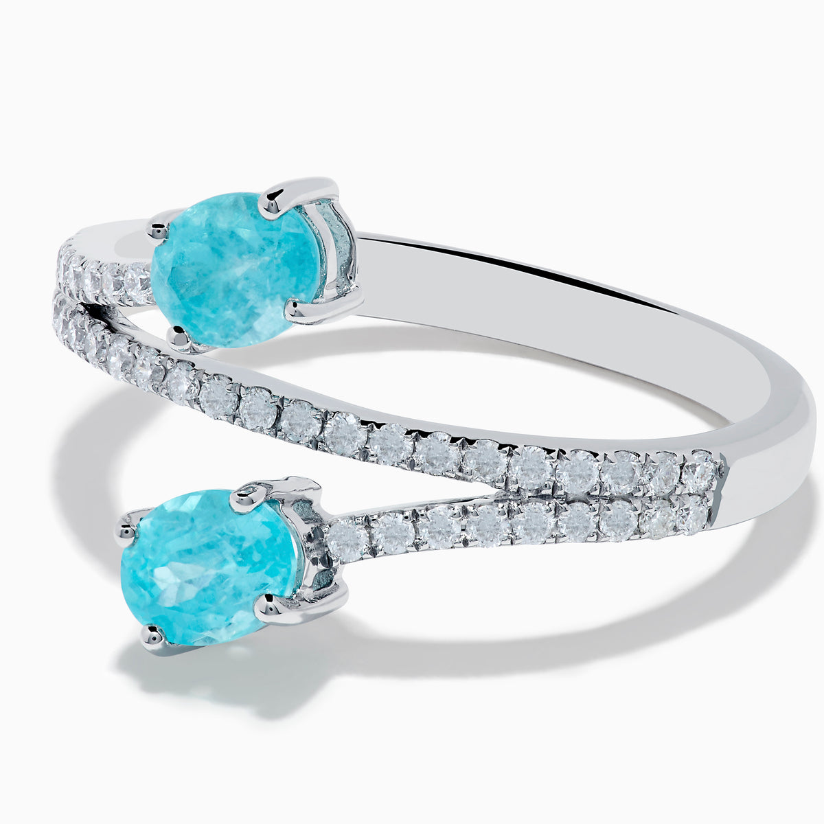 The 18K White Gold Paraiba and Diamond Bypass Ring features two oval Paraiba gemstones at each end of an open band, accented with small sparkling diamonds along the upper surface.