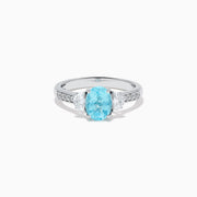The 14K White Gold Paraiba and Diamond Three Stone Ring features an oval blue Paraiba at the center, flanked by two diamonds, with additional diamonds set along each side of the band.