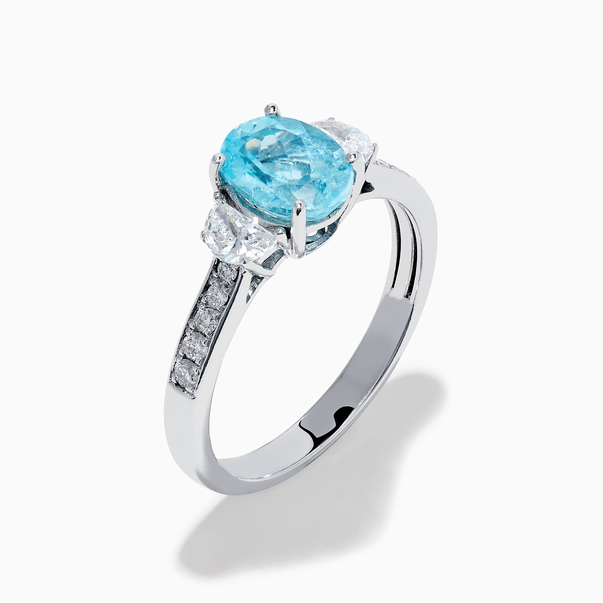 The 14K White Gold Paraiba and Diamond Three Stone Ring features an oval blue Paraiba at the center, flanked by two diamonds, with additional diamonds set along each side of the band.