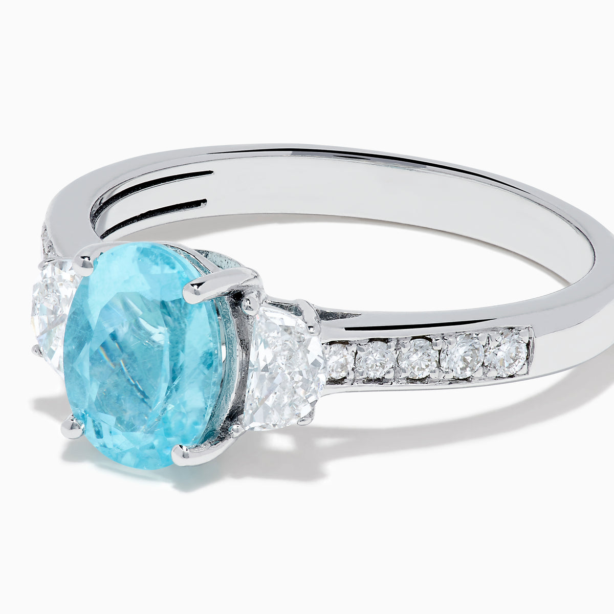 The 14K White Gold Paraiba and Diamond Three Stone Ring features an oval blue Paraiba at the center, flanked by two diamonds, with additional diamonds set along each side of the band.