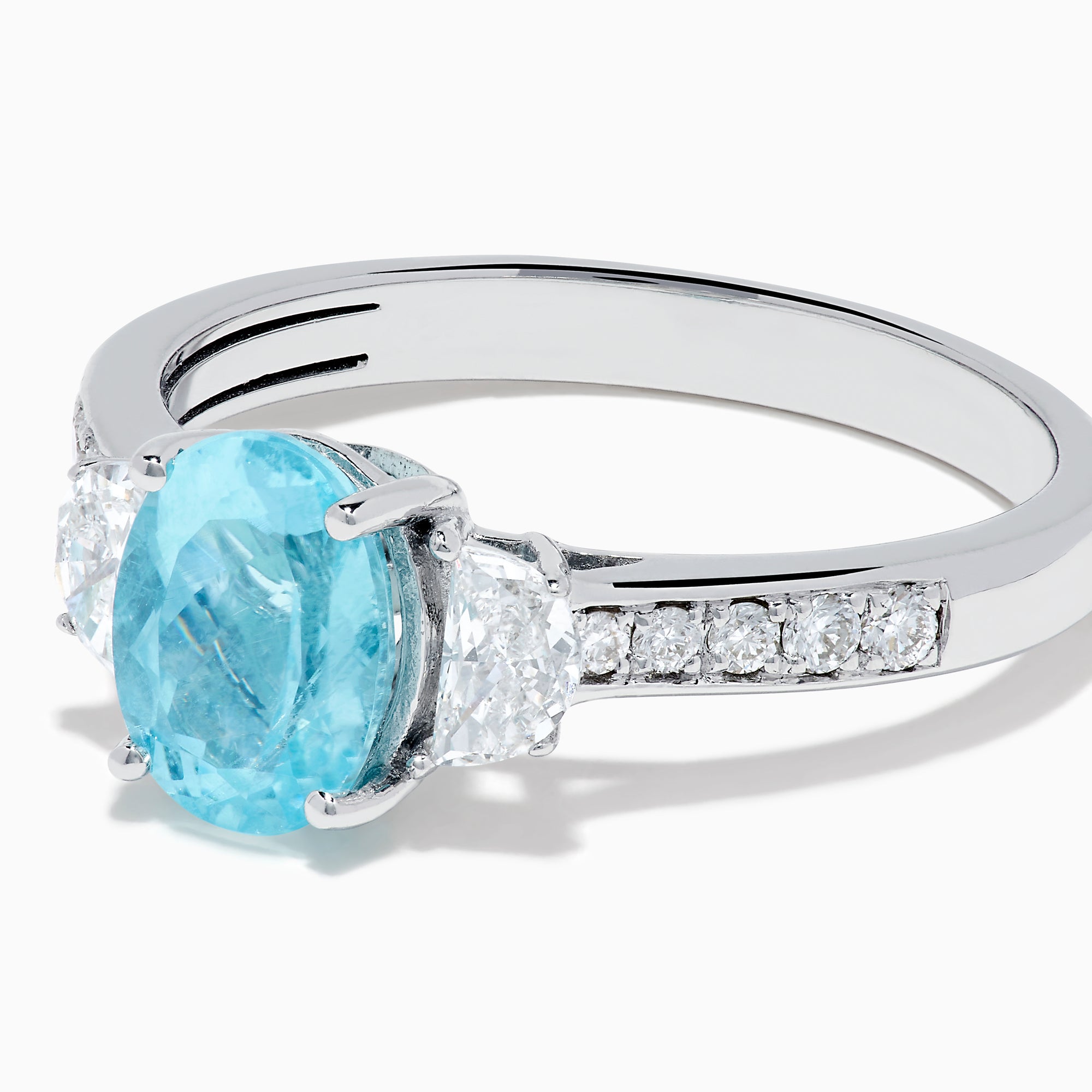 The 14K White Gold Paraiba and Diamond Three Stone Ring features an oval blue Paraiba at the center, flanked by two diamonds, with additional diamonds set along each side of the band.