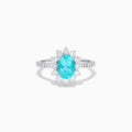 The 14K White Gold Paraiba and Diamond Halo Ring showcases an oval-shaped Paraiba gemstone at the center, encircled by a sparkling diamond halo with additional diamonds adorning the band.