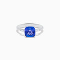 The Nahla Siri 14K White Gold Tanzanite and Diamond Ring features a striking cushion-cut blue tanzanite accented by two sparkling rectangular diamonds, elegantly displayed against a white background.