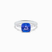 The Nahla Siri 14K White Gold Tanzanite and Diamond Ring features a striking cushion-cut blue tanzanite accented by two sparkling rectangular diamonds, elegantly displayed against a white background.