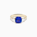 The Nahla Siri 14K Yellow Gold Tanzanite and Diamond Ring showcases a large cushion-cut tanzanite center stone, accented by two tapered white diamonds, displayed on a white background.