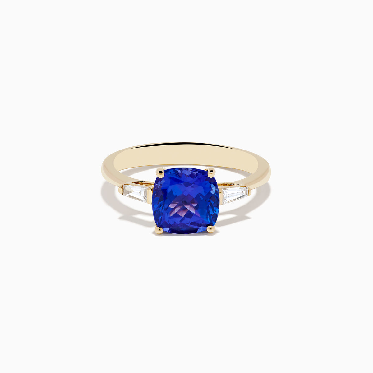 The Nahla Siri 14K Yellow Gold Tanzanite and Diamond Ring showcases a large cushion-cut tanzanite center stone, accented by two tapered white diamonds, displayed on a white background.
