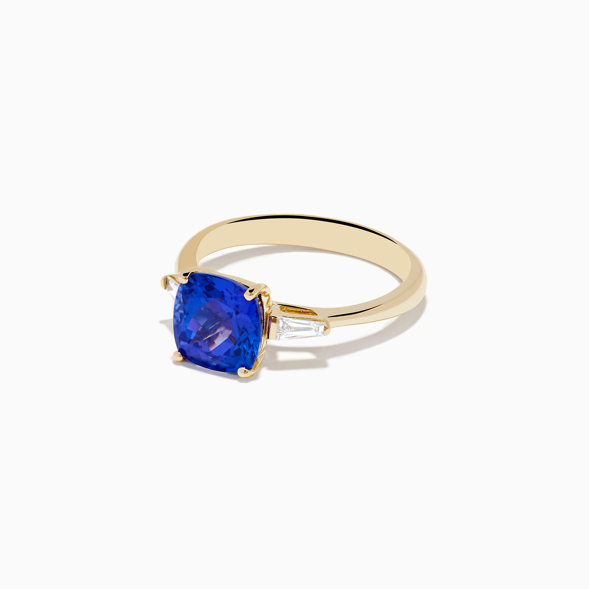 The Nahla Siri 14K Yellow Gold Tanzanite and Diamond Ring showcases a large cushion-cut tanzanite center stone, accented by two tapered white diamonds, displayed on a white background.