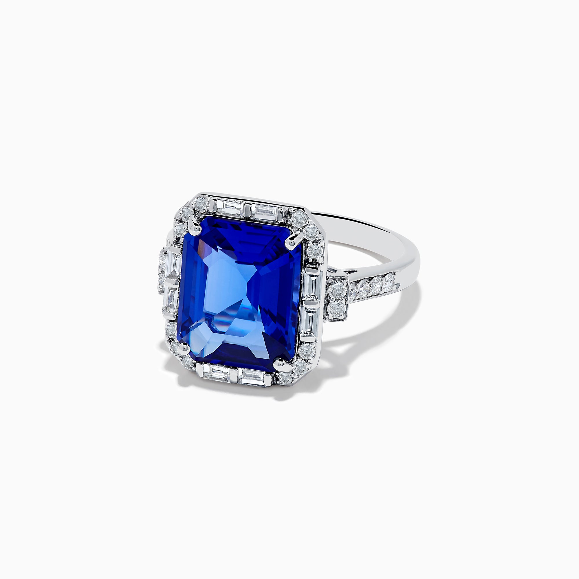 The Nahla Siri 14K White Gold Emerald Cut Tanzanite and Diamond Ring features a large emerald-cut tanzanite center, accented by baguette and round diamonds, displayed on a white background.