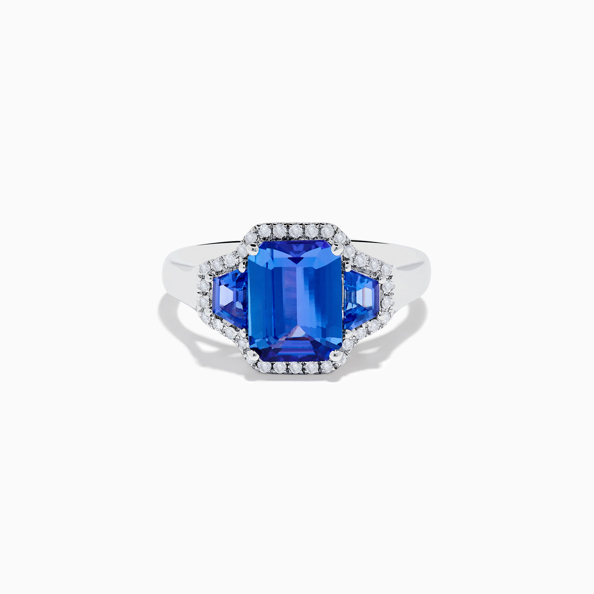 The Nahla 14K White Gold 3 Stone Tanzanite and Diamond Ring features an emerald-cut tanzanite center flanked by sparkling diamonds, all set in a geometric design and displayed on a white background.