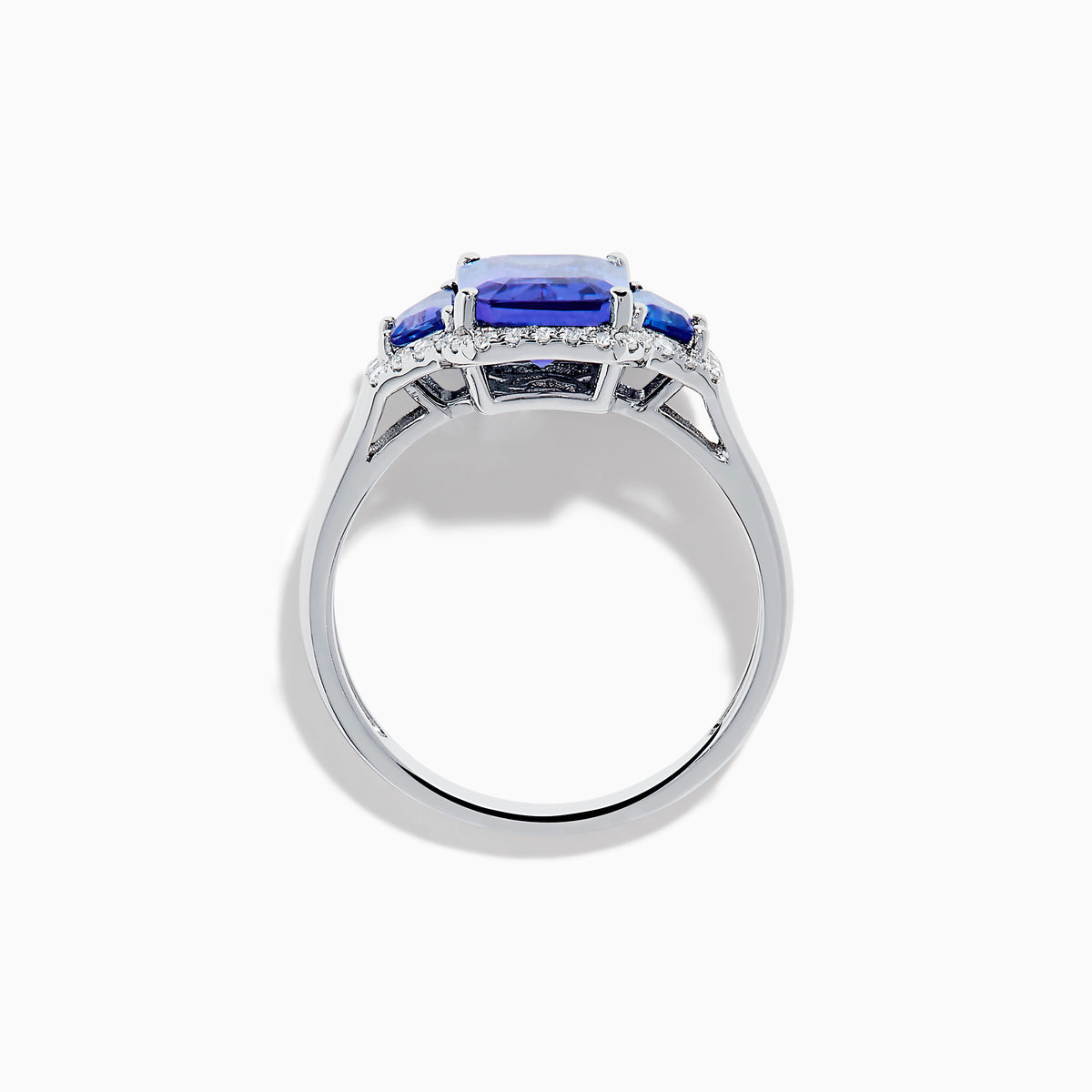 The Nahla 14K White Gold 3 Stone Tanzanite and Diamond Ring features an emerald-cut tanzanite center flanked by sparkling diamonds, all set in a geometric design and displayed on a white background.
