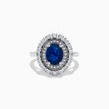The 14K White Gold Blue Sapphire and Diamond Double Halo Ring features an oval blue sapphire surrounded by two halos of round white diamonds on a white gold band, shown against a white background.