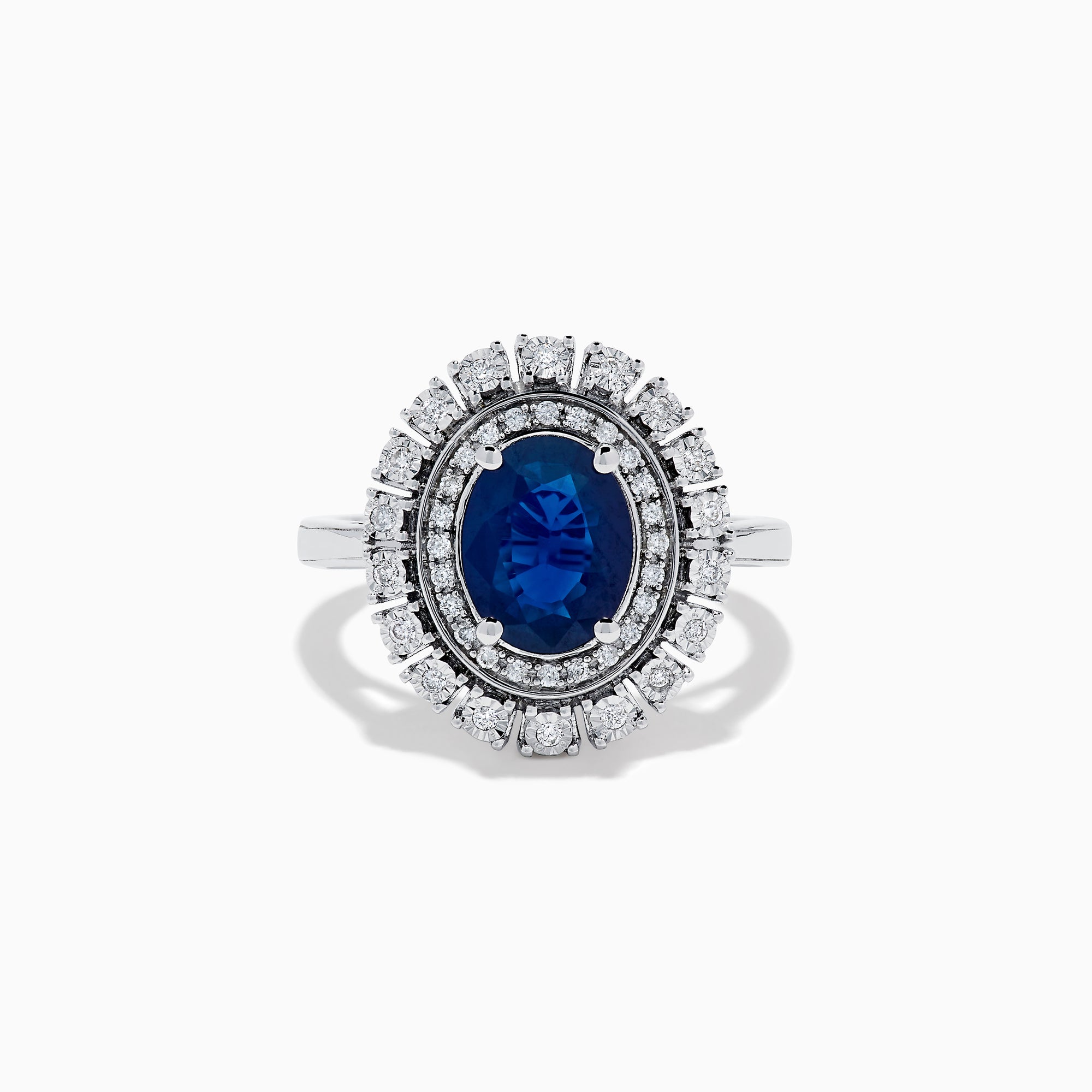 The 14K White Gold Blue Sapphire and Diamond Double Halo Ring features an oval blue sapphire surrounded by two halos of round white diamonds on a white gold band, shown against a white background.