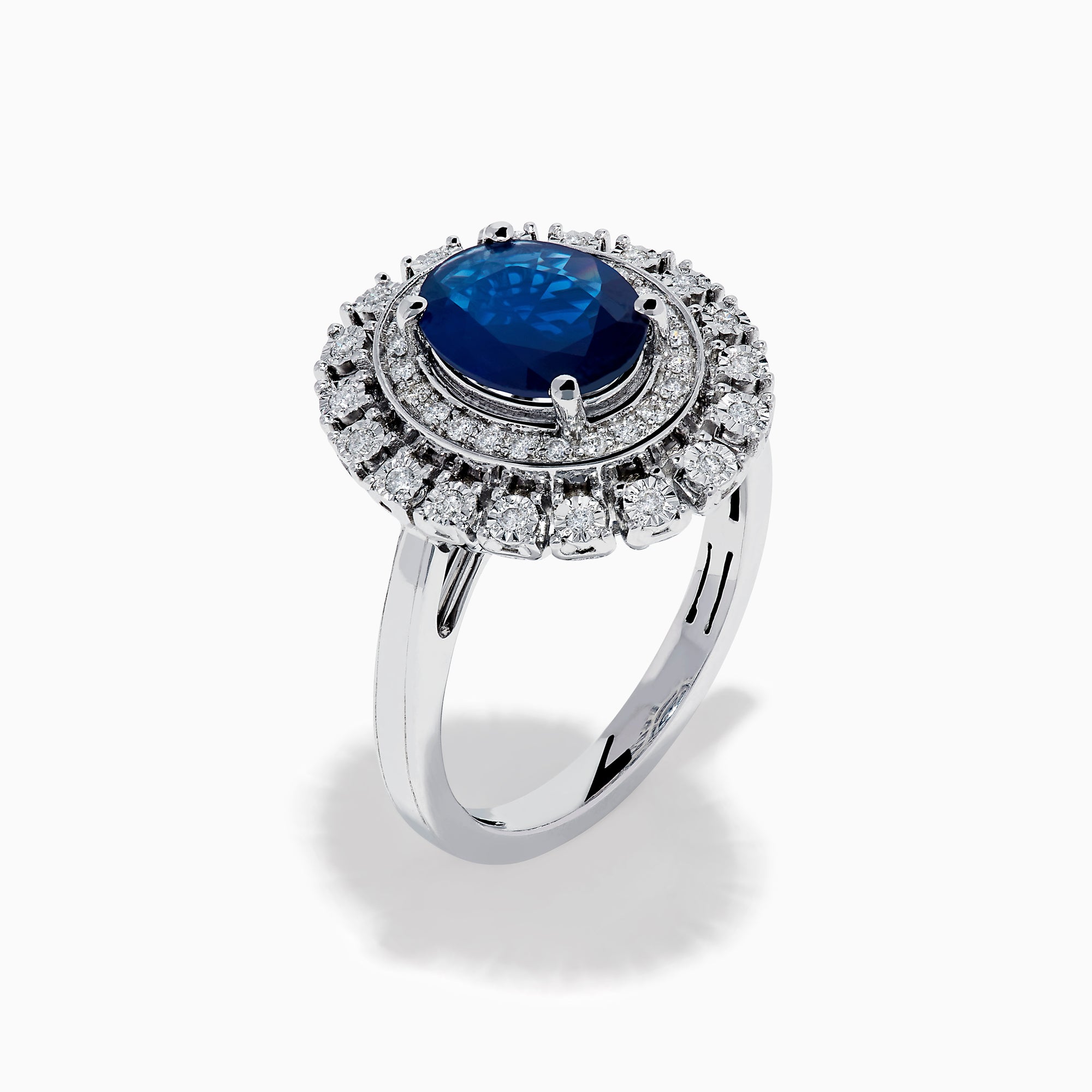 The 14K White Gold Blue Sapphire and Diamond Double Halo Ring features an oval blue sapphire surrounded by two halos of round white diamonds on a white gold band, shown against a white background.