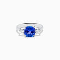 The Nahla Siri 14K White Gold Tanzanite and Diamond Ring features a large cushion-cut blue tanzanite center stone, accented by two smaller white diamonds on each side, set against a white background.