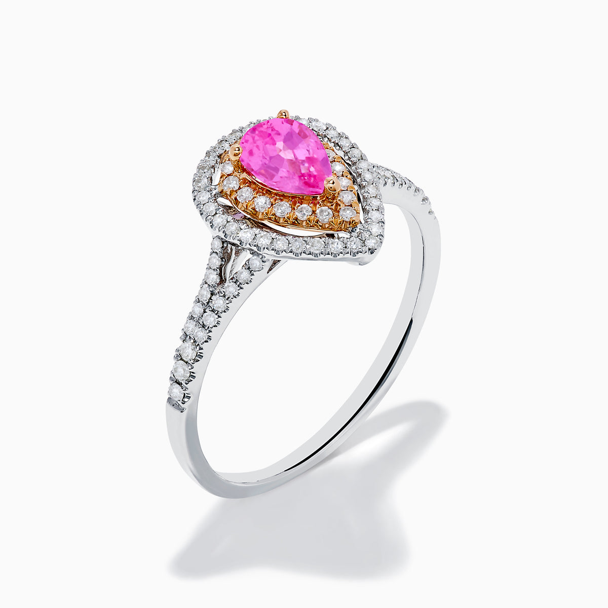 The 14K Two Tone Gold Pink Sapphire and Diamond Halo Ring showcases a pear-shaped pink sapphire center, double diamond halo with gold accents, and extra diamonds set along its two tone gold band.