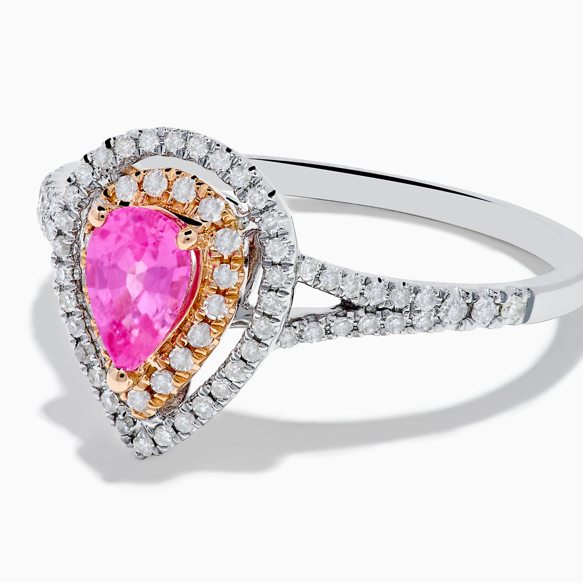 The 14K Two Tone Gold Pink Sapphire and Diamond Halo Ring showcases a pear-shaped pink sapphire center, double diamond halo with gold accents, and extra diamonds set along its two tone gold band.