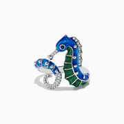 The Seaside 14K White Gold Blue Sapphire and Diamond Seahorse Ring features two seahorses with blue and green enamel details and sparkling gemstones, shown against a white background.