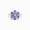 The Nahla 14K Yellow Gold Tanzanite and Diamond Flower Ring features six tanzanite petals, a center cluster of white diamonds, and extra diamonds set along the band for added sparkle.
