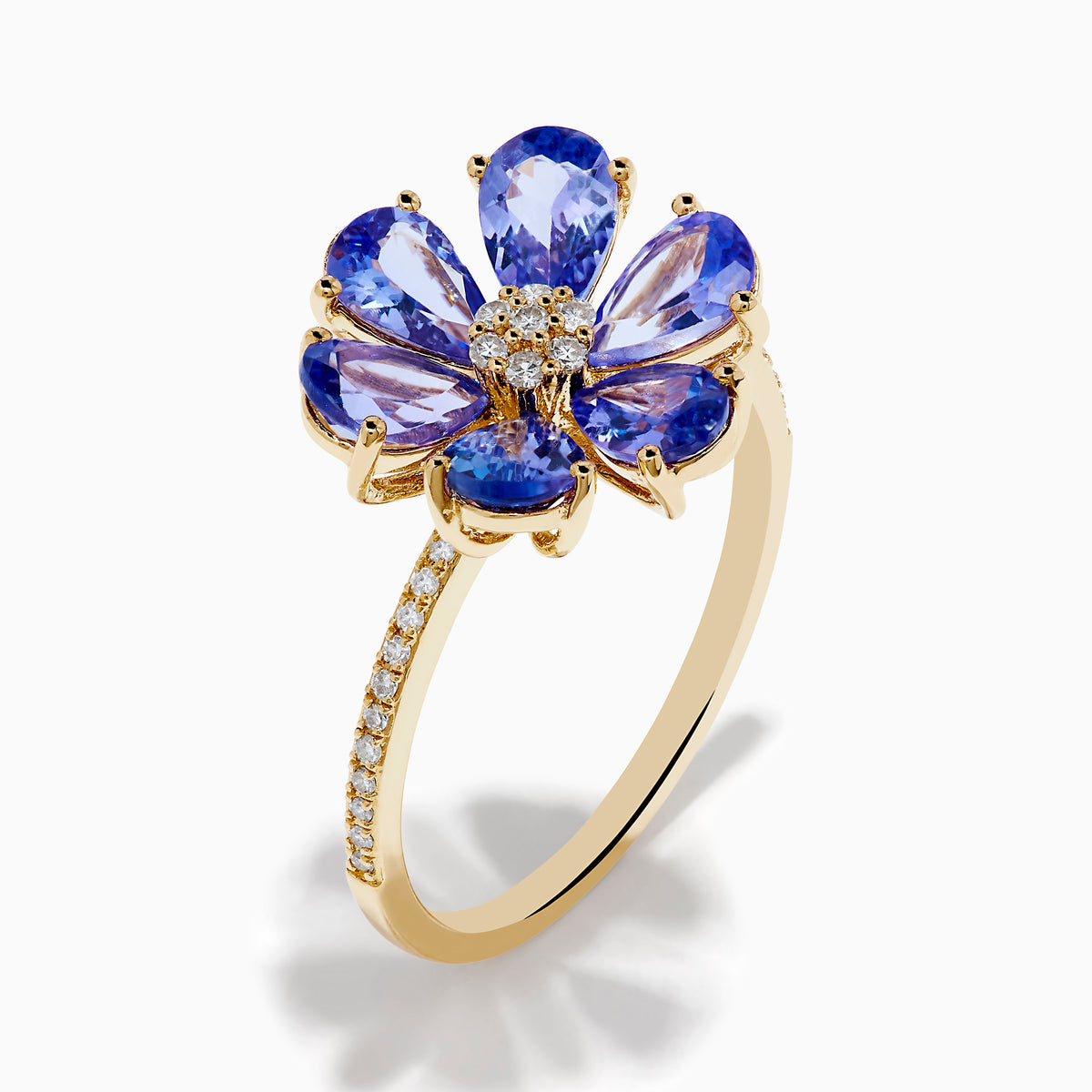 The Nahla 14K Yellow Gold Tanzanite and Diamond Flower Ring features six tanzanite petals, a center cluster of white diamonds, and extra diamonds set along the band for added sparkle.
