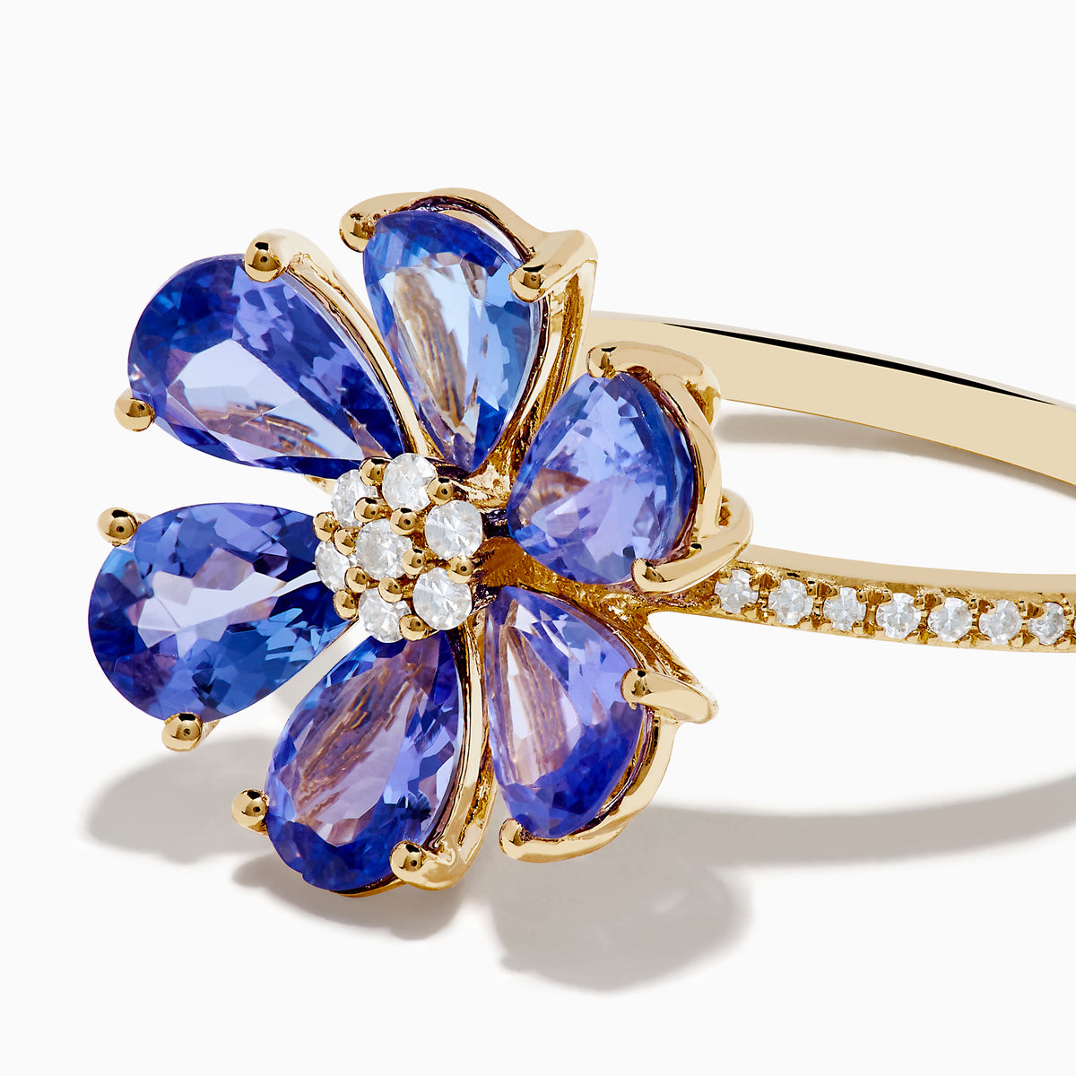 The Nahla 14K Yellow Gold Tanzanite and Diamond Flower Ring features six tanzanite petals, a center cluster of white diamonds, and extra diamonds set along the band for added sparkle.