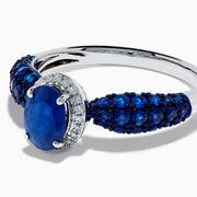 The 14K White Gold Blue Sapphire and Diamond Ring showcases a striking oval blue sapphire center, surrounded by sparkling diamonds, with additional sapphires set along the band.