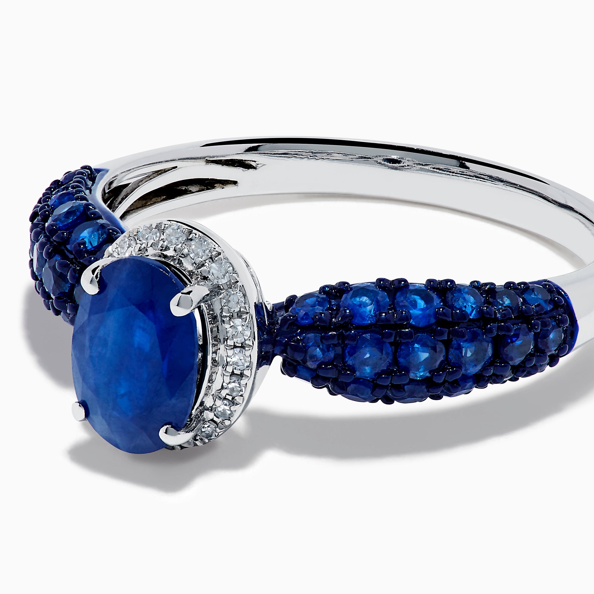 The 14K White Gold Blue Sapphire and Diamond Ring showcases a striking oval blue sapphire center, surrounded by sparkling diamonds, with additional sapphires set along the band.