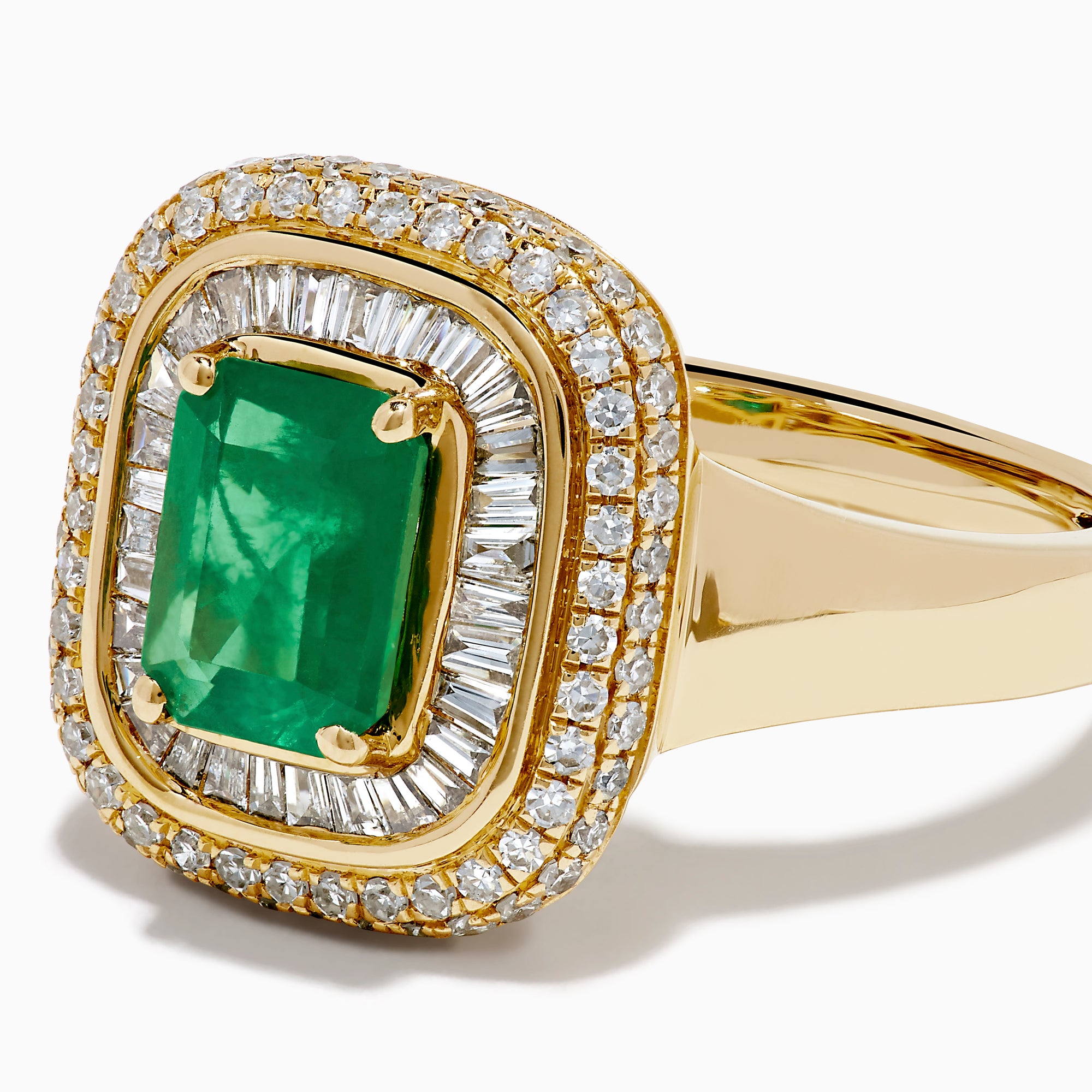 The 14K Yellow Gold Emerald and Diamond Double Halo Ring features an emerald-cut green gemstone at the center, framed by two rows of round and baguette diamonds in a rectangular halo setting.
