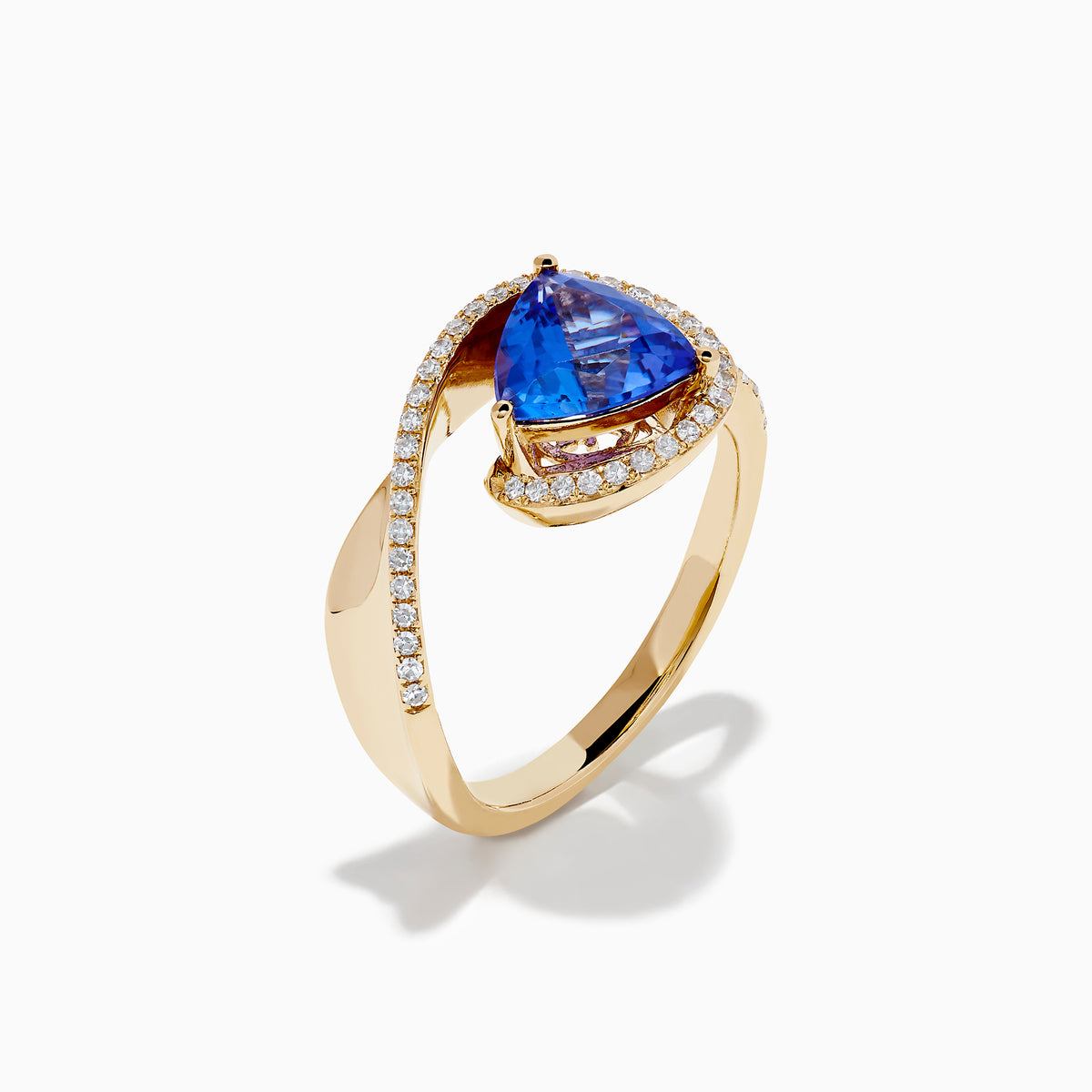 The 14K Yellow Gold Trillion Tanzanite and Diamond Swirl Ring showcases a triangular blue tanzanite center framed by a swirl of white diamonds, all set against a plain white background.