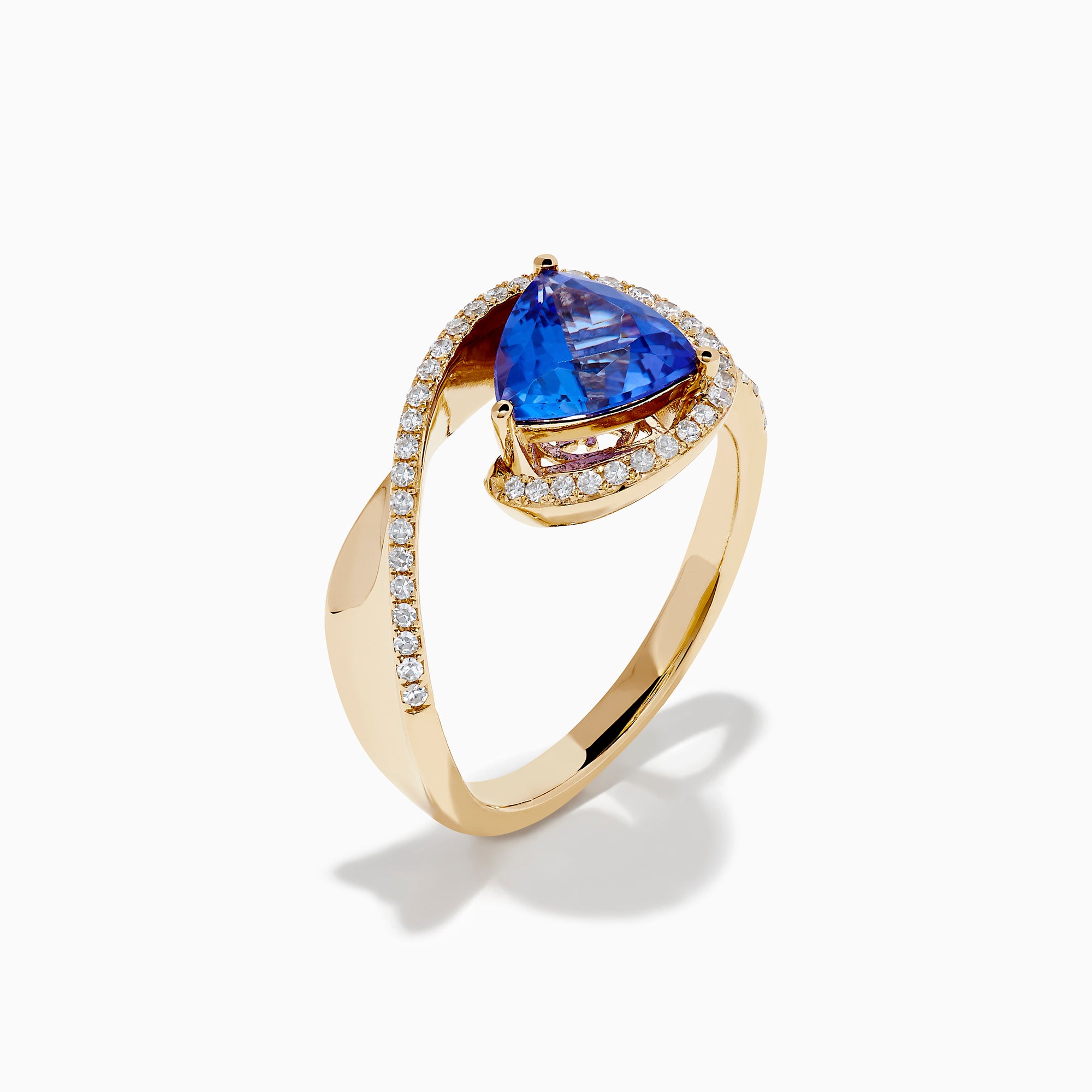 The 14K Yellow Gold Trillion Tanzanite and Diamond Swirl Ring showcases a triangular blue tanzanite center framed by a swirl of white diamonds, all set against a plain white background.