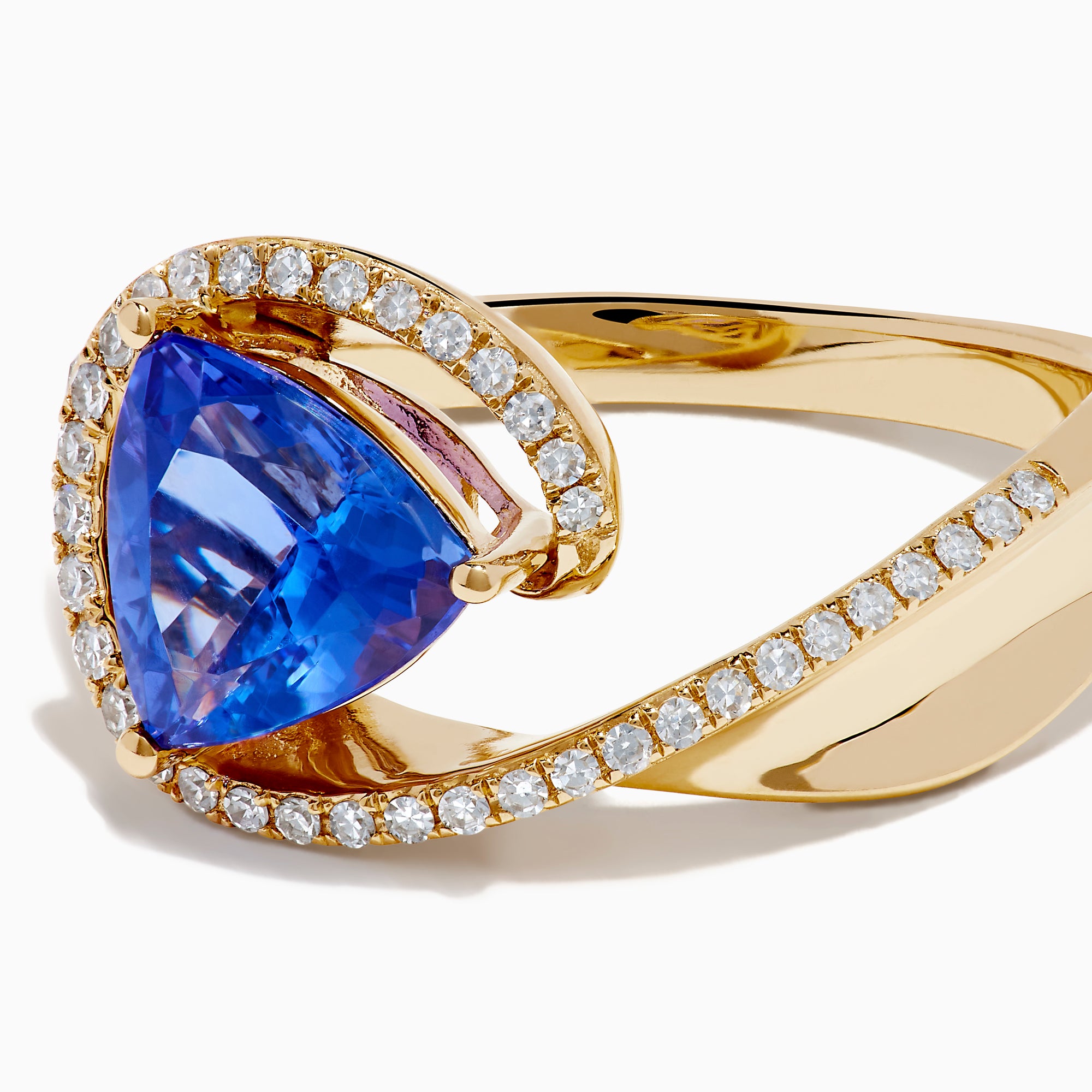 The 14K Yellow Gold Trillion Tanzanite and Diamond Swirl Ring showcases a triangular blue tanzanite center framed by a swirl of white diamonds, all set against a plain white background.