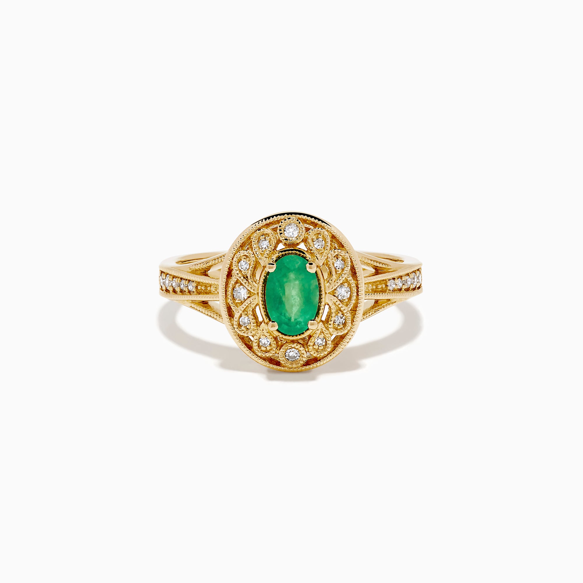 The 14K Yellow Gold Emerald and Diamond Filigree Halo Ring showcases a central oval green emerald, surrounded by a sparkling diamond halo and diamonds set along the split band.