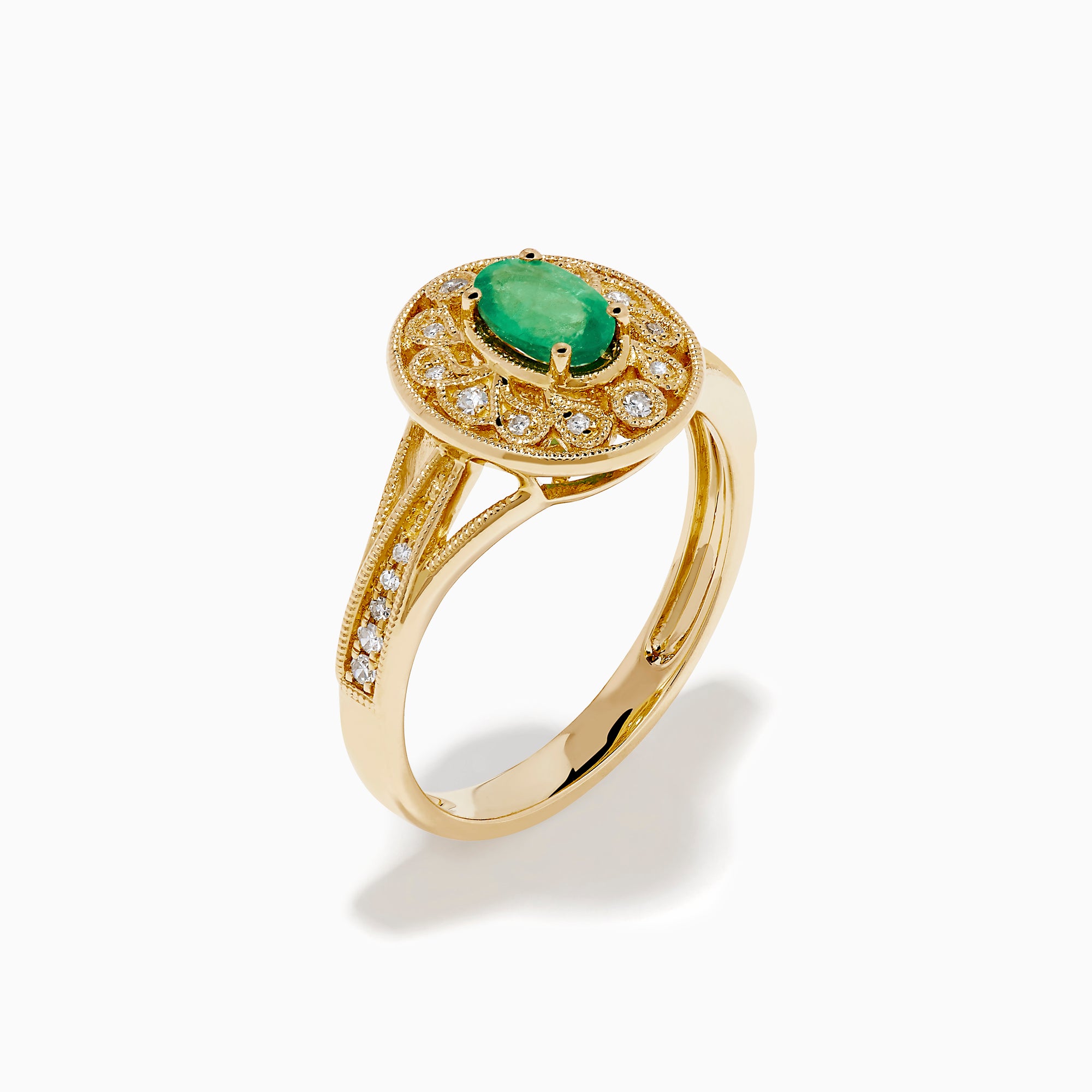 The 14K Yellow Gold Emerald and Diamond Filigree Halo Ring showcases a central oval green emerald, surrounded by a sparkling diamond halo and diamonds set along the split band.