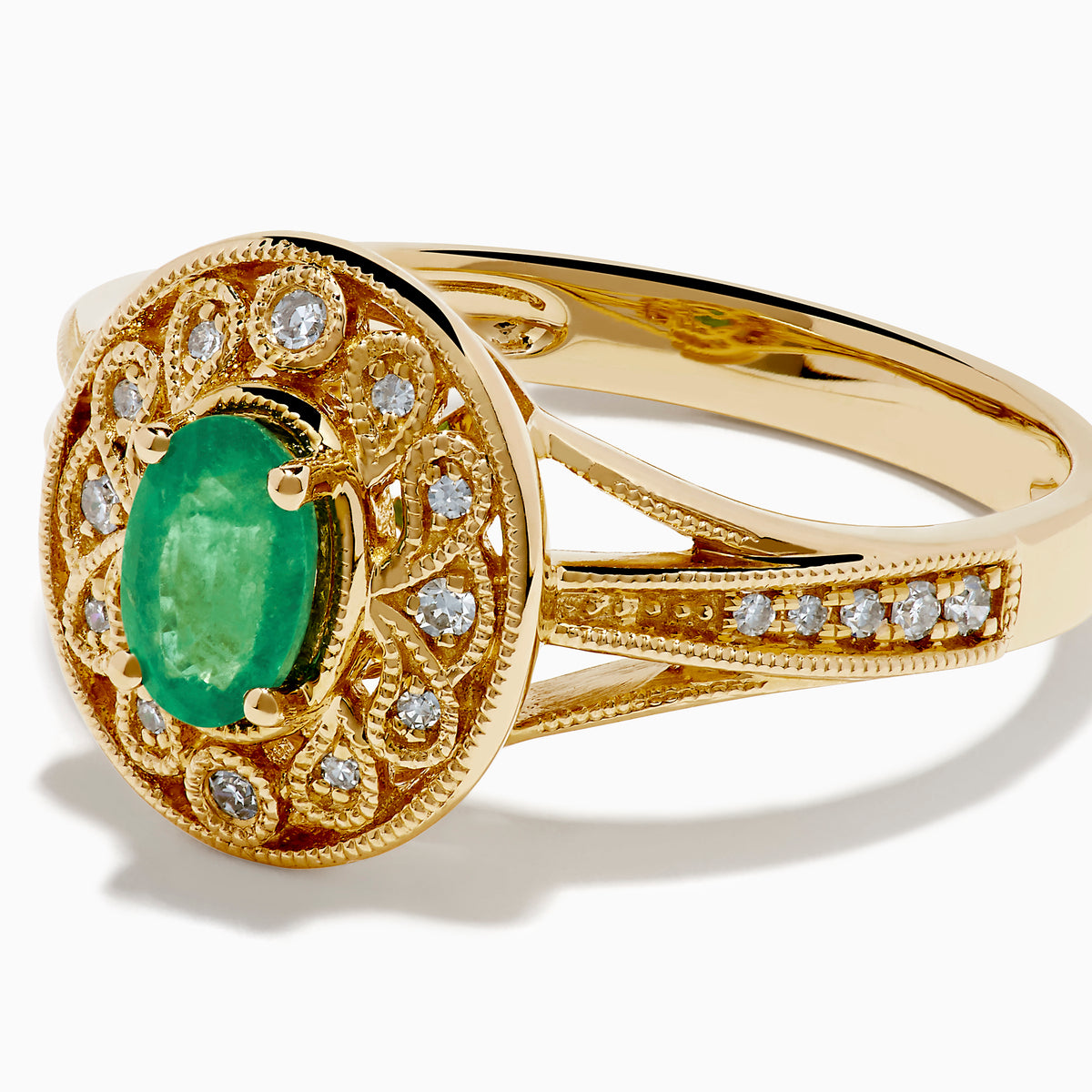 The 14K Yellow Gold Emerald and Diamond Filigree Halo Ring showcases a central oval green emerald, surrounded by a sparkling diamond halo and diamonds set along the split band.