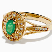 The 14K Yellow Gold Emerald and Diamond Filigree Halo Ring showcases a central oval green emerald, surrounded by a sparkling diamond halo and diamonds set along the split band.