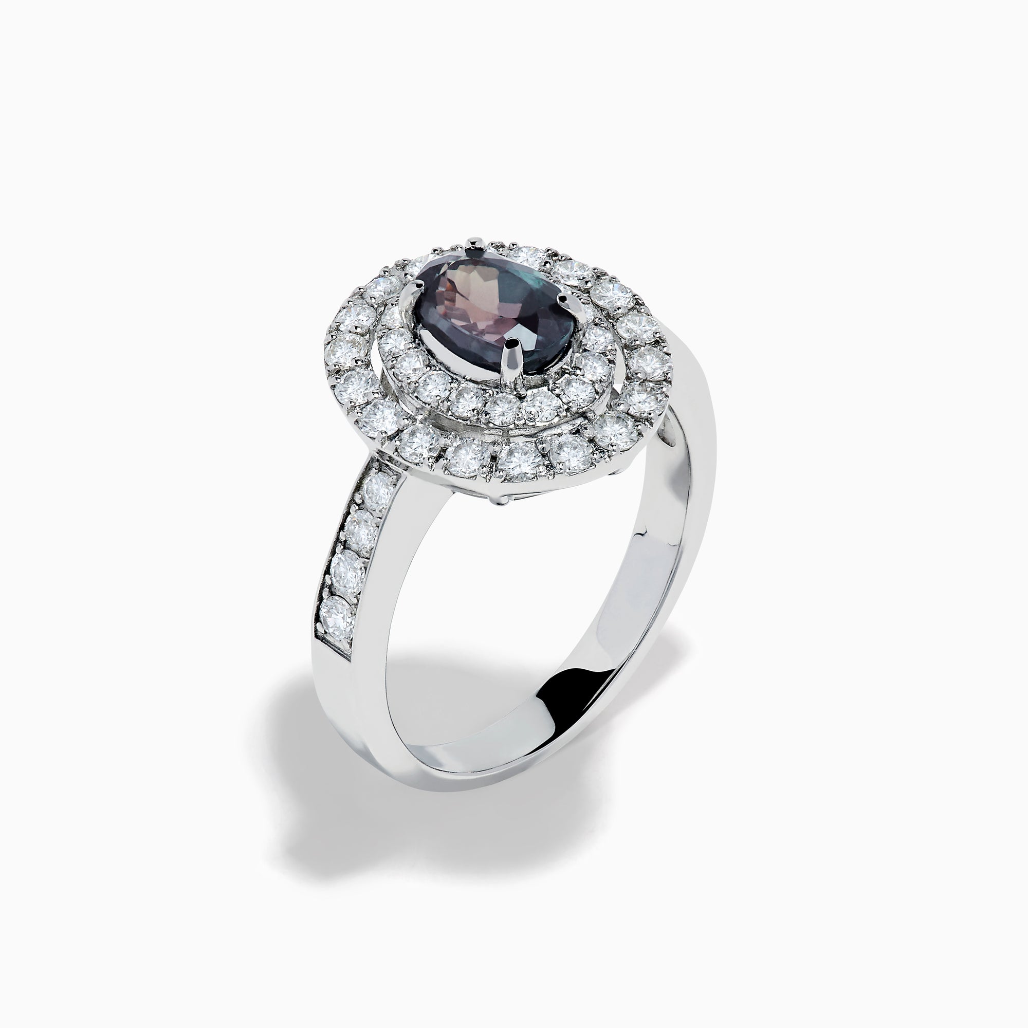 The Platinum GIA Certified Alexandrite and Diamond Double Halo Ring showcases an oval dark blue Alexandrite center stone, two rows of sparkling round diamonds in a double halo, and additional diamonds on the band, all set against a white background.