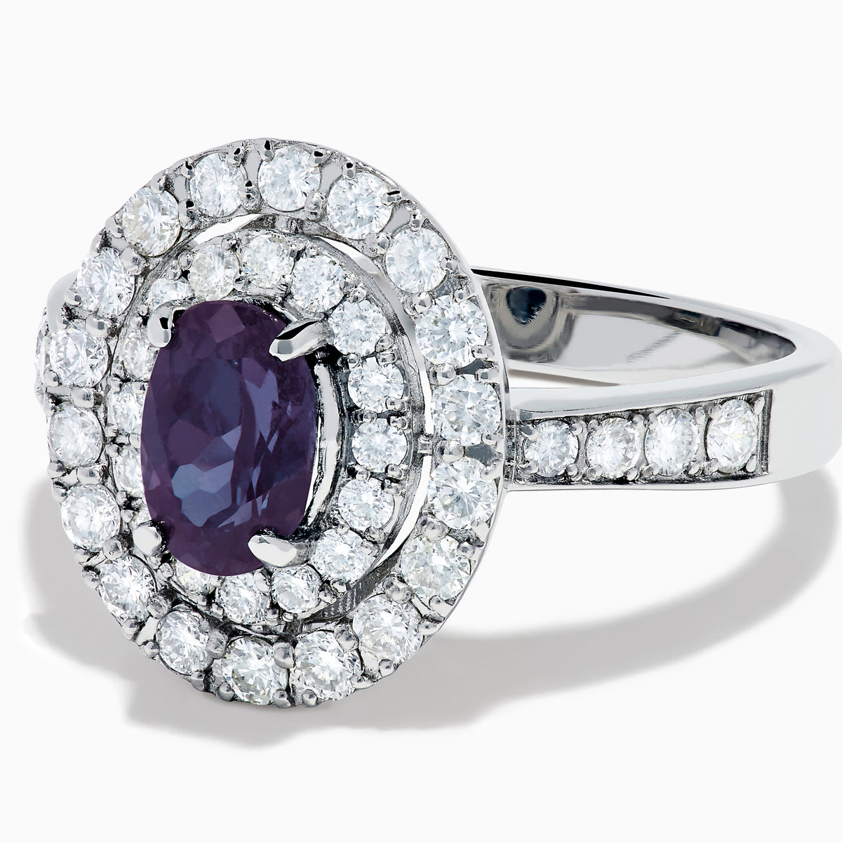 The Platinum GIA Certified Alexandrite and Diamond Double Halo Ring showcases an oval dark blue Alexandrite center stone, two rows of sparkling round diamonds in a double halo, and additional diamonds on the band, all set against a white background.
