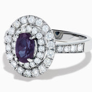 The Platinum GIA Certified Alexandrite and Diamond Double Halo Ring showcases an oval dark blue Alexandrite center stone, two rows of sparkling round diamonds in a double halo, and additional diamonds on the band, all set against a white background.
