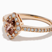 The 14K Rose Gold Brown and White Diamond Halo Ring showcases an oval brown and white diamond center, encircled by a halo of white diamonds and set with additional diamonds along the band.