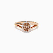 The Espresso 14K Rose Gold Brown Diamond Ring features an oval light brown diamond surrounded by a halo of small white diamonds and set on a twisted rose gold band.