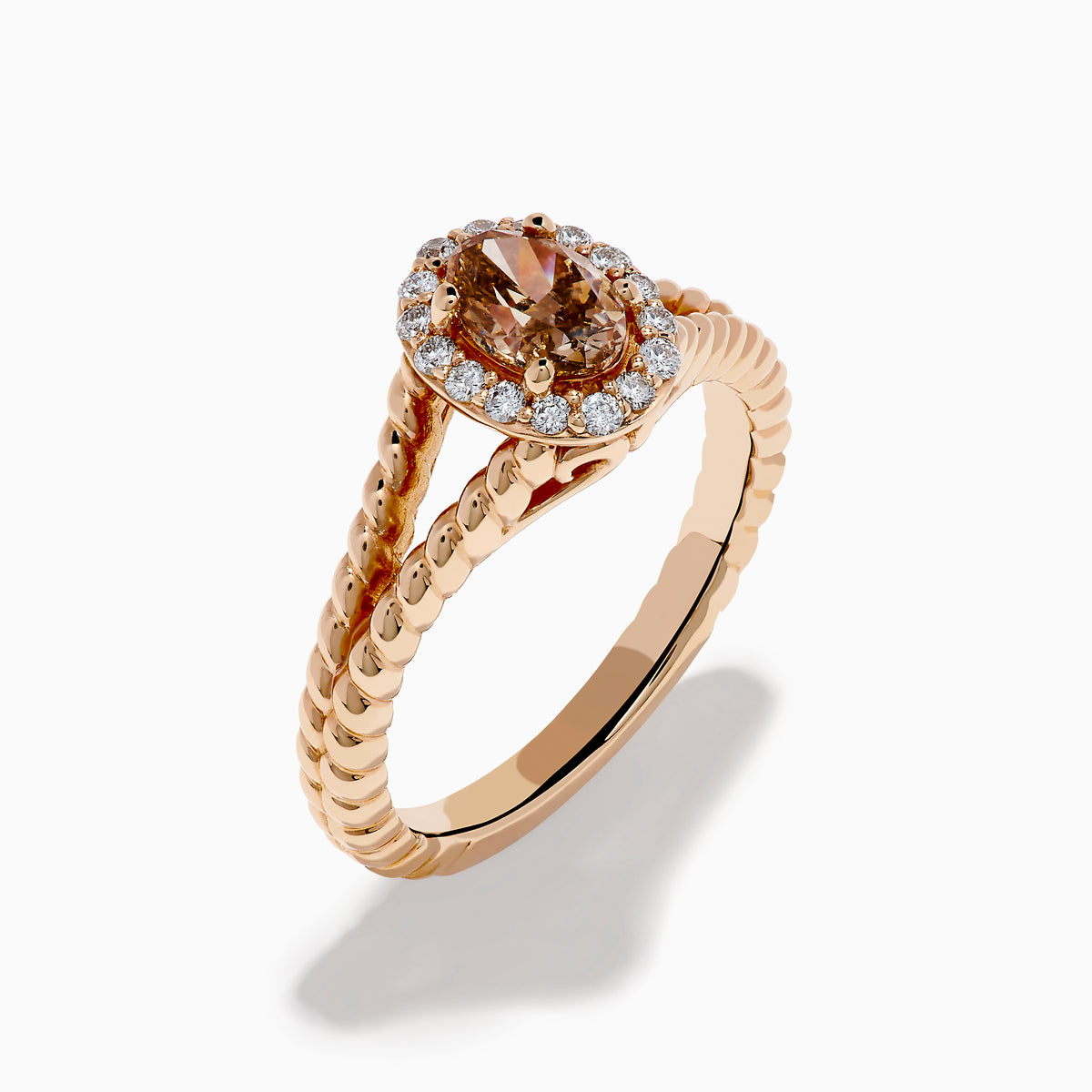 The Espresso 14K Rose Gold Brown Diamond Ring features an oval light brown diamond surrounded by a halo of small white diamonds and set on a twisted rose gold band.