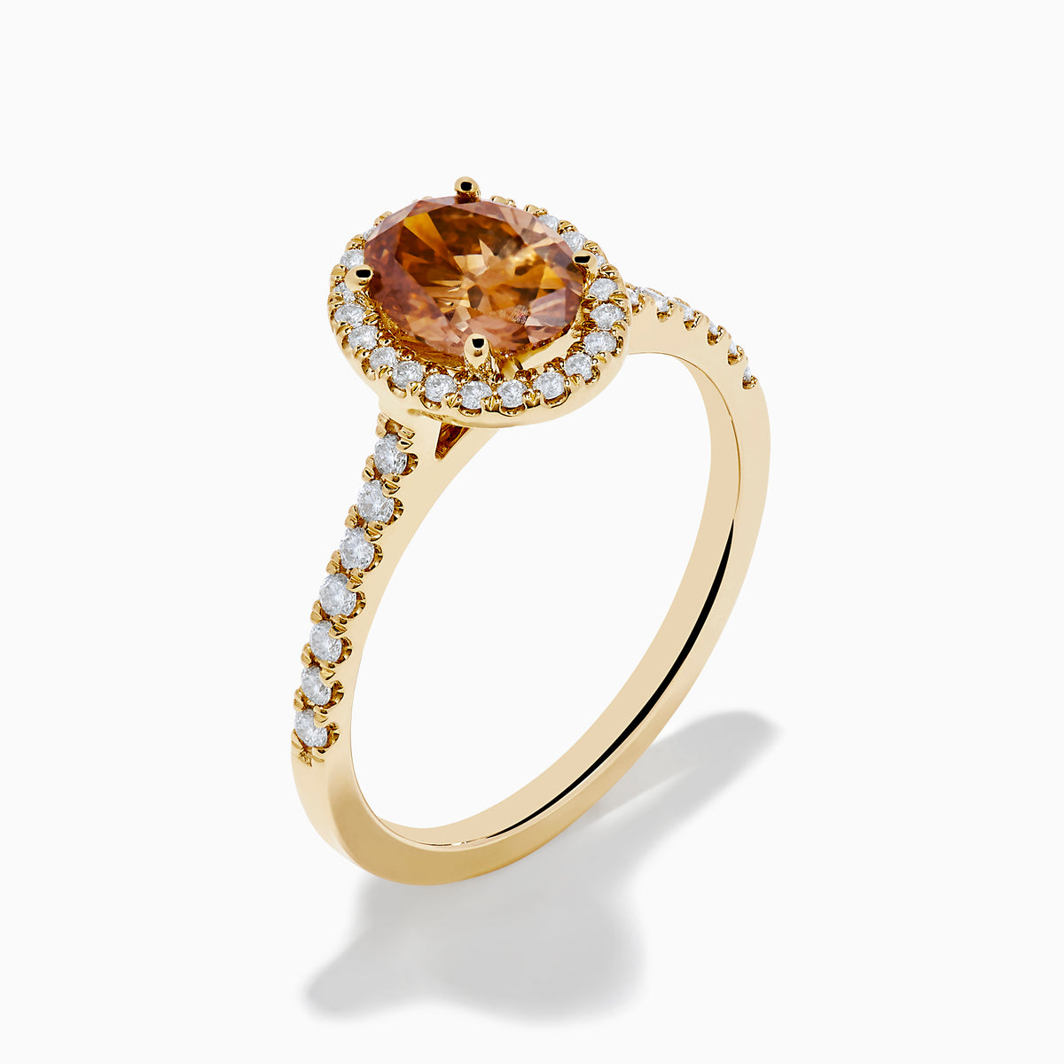 The Espresso 14K Yellow Gold Brown Diamond Halo Ring showcases an oval brown diamond center, encircled by a halo of white diamonds with additional diamonds set along the band.