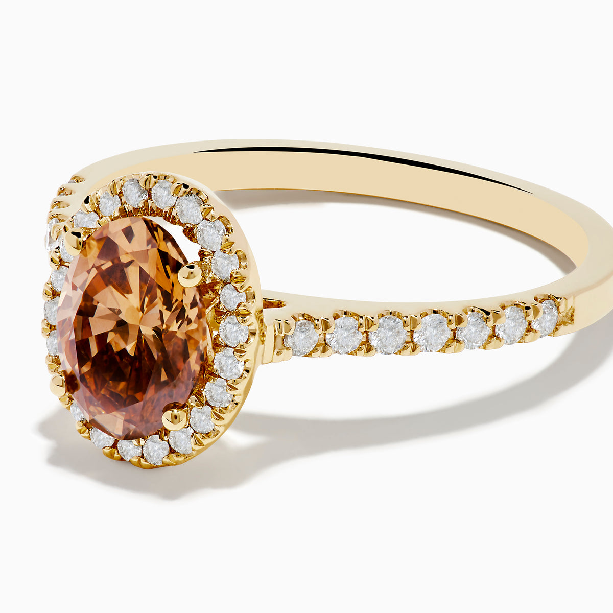 The Espresso 14K Yellow Gold Brown Diamond Halo Ring showcases an oval brown diamond center, encircled by a halo of white diamonds with additional diamonds set along the band.