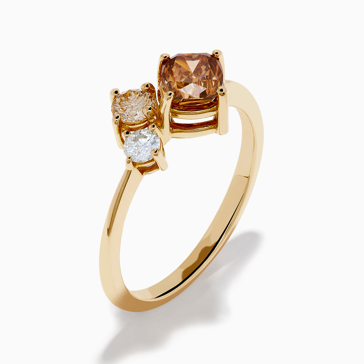 The Espresso 14K Yellow Gold Brown and White Diamond Ring showcases a round white diamond, a pear-shaped light brown diamond, and a cushion-cut brown diamond in a minimalist design against a white background.