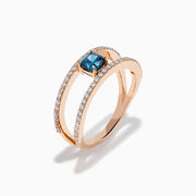 The Bella Bleu 14K Rose Gold Blue and White Diamond Ring features two parallel, diamond-encrusted bands and a cushion-cut blue gemstone centerpiece. This modern, elegant ring stands out beautifully against a crisp white background.