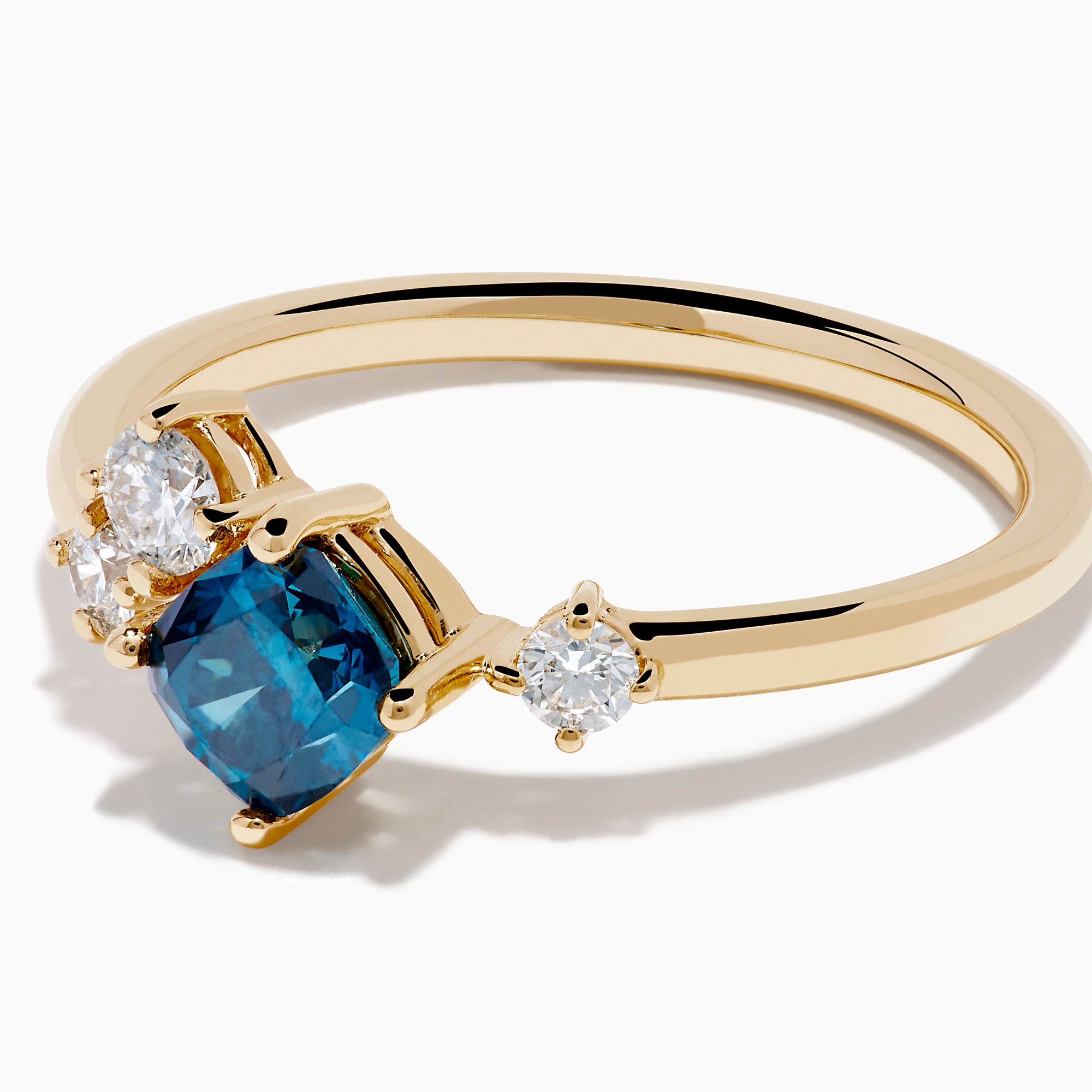The 14K Yellow Gold Blue and White Diamond Ring showcases a cushion-cut blue stone center with two round white diamonds on each side, set against a white background.