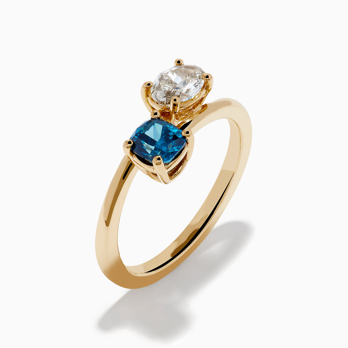 The Bella Bleu 14K Yellow Gold Blue and Light Brown Bypass Diamond Ring showcases an oval white diamond and a cushion-cut deep blue gemstone set side by side on a sleek gold band.