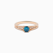 The Bella Bleu 14K Rose Gold Blue and White Diamond Ring showcases a blue rectangular gemstone at the center with small round white diamonds on each side, set against a plain white background.