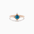 The Bella Bleu 14K Rose Gold Blue and White Diamond Ring features a cushion-cut blue gemstone at its center, accented by four symmetrically placed round white diamonds.