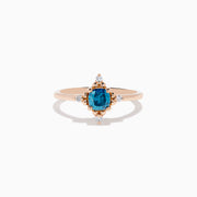 The Bella Bleu 14K Rose Gold Blue and White Diamond Ring features a cushion-cut blue gemstone at its center, accented by four symmetrically placed round white diamonds.