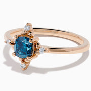 The Bella Bleu 14K Rose Gold Blue and White Diamond Ring features a cushion-cut blue gemstone at its center, accented by four symmetrically placed round white diamonds.